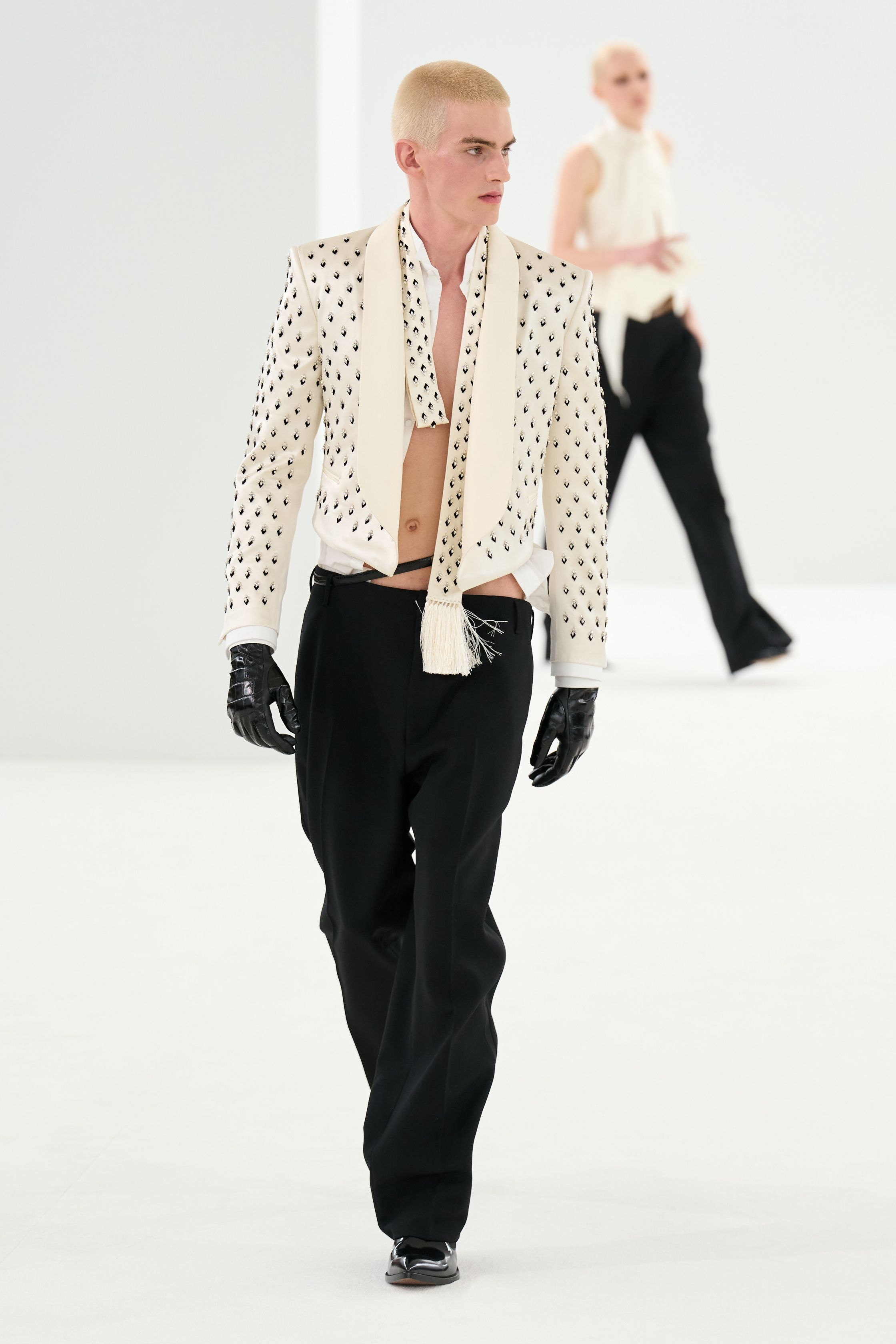 Tom Ford 2026秋冬系列回归品牌标志性的性感极简主义。高腰铅笔裙、透明材质层叠与利落西装展现强烈的都市魅力。黑色、棕色与金属光泽构成成熟而冷峻的色彩体系，皮革与光泽面料的运用强化性感张力。整体造型强调身体线条与权力感，展现Tom Ford一贯的夜晚都市美学-顽石频道趋势研究